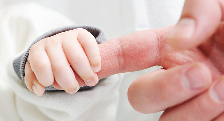 En bebishand kramar om ett finger. Foto.