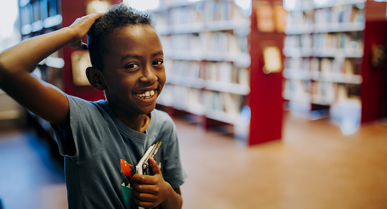 Ett barn håller i en bok på ett bibliotek. Foto.