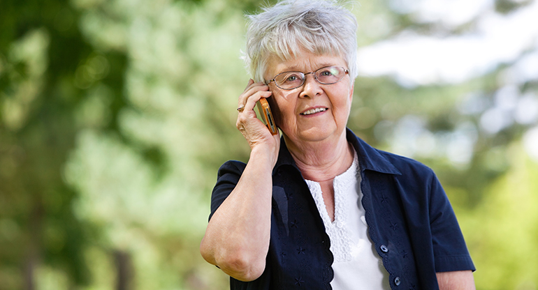 Äldre kvinna prata i telefon utomhus. Foto.