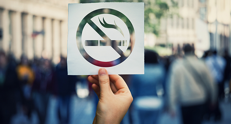 En hand håller upp en skylt med rökning förbjuden. Foto.