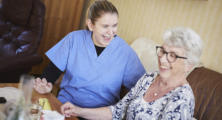 En kvinna som jobbar inom hemtjänsten skrattar tillsammans med en äldre kvinna. Foto.