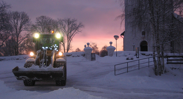 Traktor som skottar snö i gryningen framför kyrkan i Åseda. Foto.