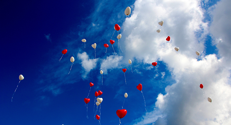 Ballonger i form av röda och vita hjärtan uppe i skyn. Foto.