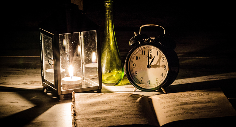 Ljuslykta, en grön flaska, en väckarklocka och en bok. Foto.